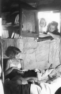Milano. Baracche. Una donna a letto legge un libro. Dalla finestra la guardano due altre donne.