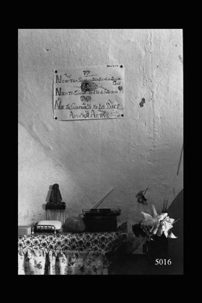 Interno di abitazione eritrea. Oggetti simbolici sopra una mensola. Cartello con messaggio augurale alla parete.