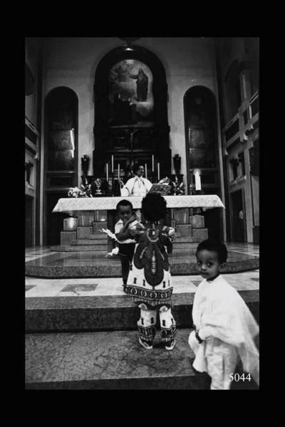 Eritrei a Milano. Cerimonia religiosa. Bambini sui gradini che portano all'altare dietro al quale padre Marino celebra la funzione religiosa.