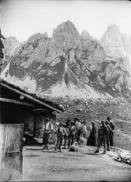 Cascina alta Campelli con gruppo - Gruppo di montanari con al centro coppia in abiti borghesi.  Sullo sfondo cime montuose  a sinistra parte della cascina.