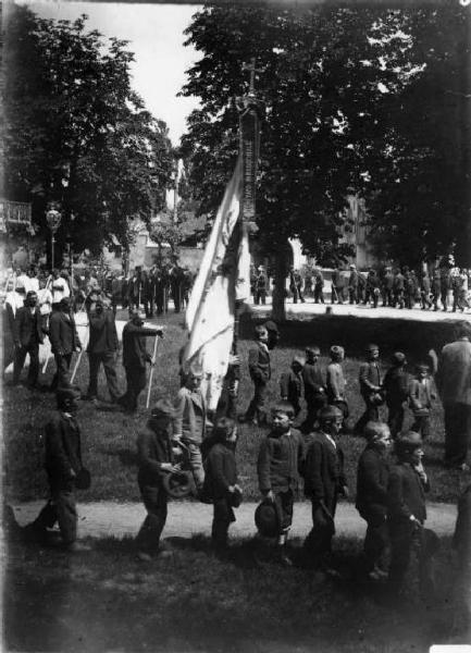 Ghedi - Processione. Parte della processione con bamini e anziani che reggono una bandiera sul cui fiocco si legge "Comitato Parrocchiale.