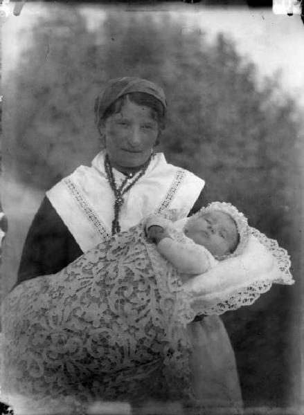 Ritratto di neonata posata su guanciale bianco ricamato sorretta dalla balia.
