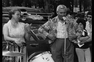 Spettacolo di cantastorie pavesi in piazza del Cannone a Milano. I cantastorie Vincenzina Cavallini e Angelo Cavallini in una fase dello spettacolo. Angelo Cavallini indossa una giacca da clown.
