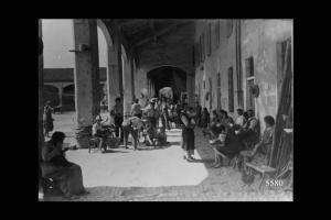 Le famiglie contadine (uomini, donne, bambini), consumano il pasto pomeridiano sotto al portico, davanti alle proprie abitazioni.
