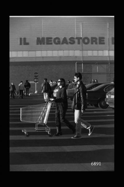 Centro commerciale di Corsico. Giovane coppia con carrello nell'area di parcheggio. Provinciale Vigevanese.