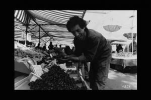 Milano, mercato di via Papiniano. Venditore ambulante di ortaggi mentre solleva manciata di duroni.