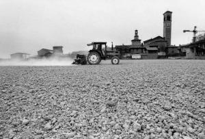 Azienda agricola: Cascina S. Antonio. Coltivazione: granoturco. Semina. Campo arato con macchina agricola da semina: sullo sfondo il paese.