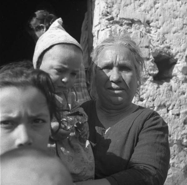 Melissa (Crotone) - Anziana donna con bambino in braccio e altri bambini sull'uscio di una casa