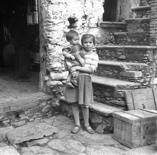 Melissa (Crotone) - Bambina con bambino più piccolo in braccio all'esterno di una casa