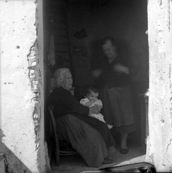 Melissa (Crotone) - Anziana donna con bambino in braccio e altra donna sull'uscio di una casa