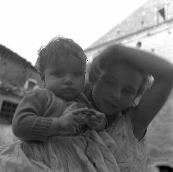 Melissa (Crotone) - Bambina con bambina più piccola in braccio in una strada