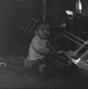 Melissa (Crotone) - Bambino piccolo seduto a terra in un interno di casa