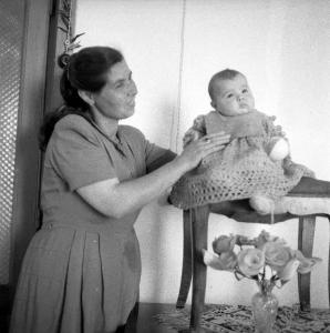 Melissa (Crotone) - Donna con bambino piccolo seduto su uno sgabello in un interno di casa