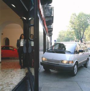 Automobile parcheggiata sul marciapiedi accanto alla vetrina di un autosalone con adulta in posa