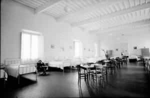 Ospedale psichiatrico - Salone - Dormitorio - Donna seduta su sedia dondolo - Tavoli
