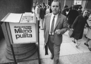 Uomo adulto accanto a un cestino recante la scritta "Milano Pulita"