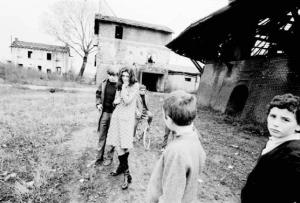Ragazzo e ragazza in un campo circondati da ragazzini che osservano - Sullo sfondo alcune cascine