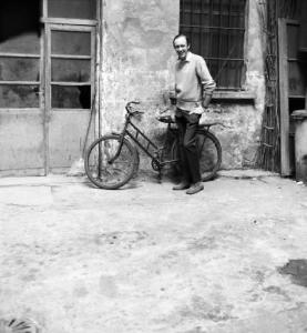 Milano - Giovane uomo sorridente con bicicletta appoggiata al muro scrostato di un cortile