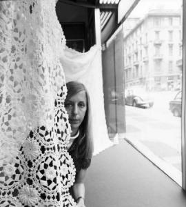 Ritratto di giovane donna dietro una tovaglia ricamata in una vetrina di negozio