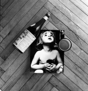 Fotografia di una bambina appoggiata sul parquet con bottiglia d'acqua e acqua rovesciata