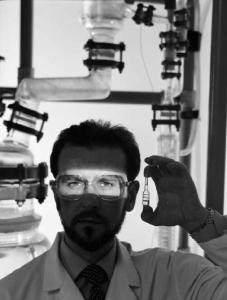 Glaxo - Ritratto di ricercatore con fiala in mano e raggio di luce sugli occhi - sullo sfondo tubi trasparenti del laboratorio