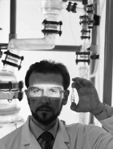 Glaxo - Ritratto di ricercatore con fiala in mano e raggio di luce sugli occhi - sullo sfondo tubi trasparenti del laboratorio