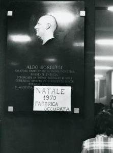 Bassorilievo che rappresenta il profilo di Aldo Borletti, sul quale è stato appoggiato un cartello con la scritta "NATALE 1970 FABBRICA OCCUPATA"