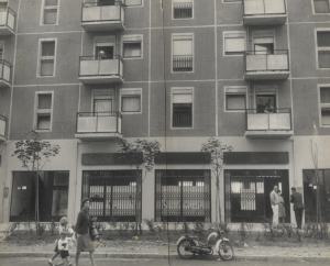 Milano - Quartiere Gratosoglio - Palazzi di edilizia popolare - Pianterreno con vetrine sulla strada - Ingresso della scuola elementare in un negozio - Mamma con bambini - Motocicletta - Commessi scolastici