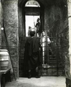 Scena del film "Fabiola" - Regia Alessandro Blasetti, 1949 - Elisa Cegani si tiene con la mano destra a una grata su una scalinata mentre fissa davanti a se un attore non identificato di spalle. Sullo sfondo degli attori non identificati.