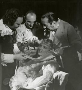 Sul set del film "La fanciulla di Portici" - Regia Bonnard, Mario, 1940 - Giuditta Rissone siede al centro mentre intorno a lei il regista Mario Bonnard le toglie le bende dal viso insieme ad altri due attori non identificati.








