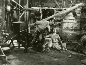 Scena del film "Il fanciullo del West" - Regia Ferroni, Giorgio, 1942 - Erminio Macario, in piedi al centro, è intento a muoversi verso destra, spostando un trabiccolo di funi e legna, che lo tiene prigioniero.