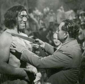 Sul set del film "La figlia del corsaro verde" - Guazzoni, Enrico, 1940 - Il regista Enrico Guazzoni, a destra, appoggia un oggetto non identificato alla spalla destra di Primo Carnera che lo osserva ridendo.
