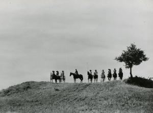 Scena del film "La figlia di Mata Hari" - Merusi, Renzo, 1954 - Sulla cima di una collina, una schiera di attori non identificati a cavallo alla destra di un albero sono rivolti verso l'obbiettivo.
