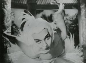 Scena del film "La figlia di Mata Hari" - Merusi, Renzo, 1954 - Primo piano di un'attrice non identificata truccata e in abiti di scena piumati in posa plastica di danza classica.
