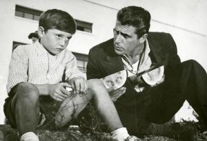 Scena del film "La finestra sul luna park" - Comencini, Luigi, 1957 - Gastone Renzelli, a destra, tiene in mano una fetta d'anguria e ne porge un'altra a un giovane attore non identificato a sinistra che rivolge lo sguardo dritto davanti a sé.

