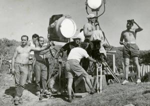 Sul set del film "La finestra sul luna park" - Comencini, Luigi, 1957 - In un ambiente di campagna, intorno a due grandi fari e a una macchina da presa, numerosi operatori non identificati lavorano.
