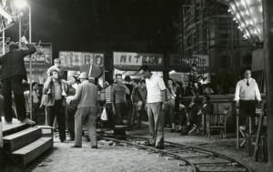 Sul set del film "La finestra sul luna park" - Comencini, Luigi, 1957 - Operatori non identificati riprendono, con una macchina da presa su rotaie, Gastone Renzelli, al centro, che parla con il giovane attore non identificato che tiene in spalla.
