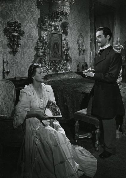 Scena del film "Giacomo l'idealista" - Lattuada, Alberto, 1942 - In una stanza da letto: Tina Lattanzi, in vestaglia seduta con un ventaglio nella mano destra e Andrea Checchi, in piedi a destra. I due attori si guardano.