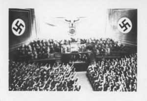 Nazismo - Germania, Berlino - Reichstag, interno - Seduta: Hitler (al centro) parla - Saluto nazista - Croce uncinata, svastica e aquila nazista