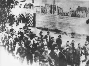 Seconda guerra mondiale - Francia, Compiégne - Campo di internamento e di transito di Royallieu - Deportazione di prigionieri verso il campo di concentramento di Dachau - Uomini in marcia scortati da SS in divisa - Muro - Nazismo