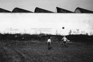 Scritte murali. Sesto San Giovanni (?) - Paesaggio industriale - Fabbrica - Capannoni - Muro di cinta - Scritte murali - Prato - Bambini - Gioco del calcio
