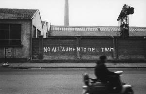 Scritte murali. Milano (?) - Paesaggio industriale - Fabbrica - Capannoni - Muro di cinta - Scritta murale - Uomo in vespa