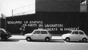 Scritte murali. Milano (?) - Muro - Scritta murale - Auto parcheggiate - Passante