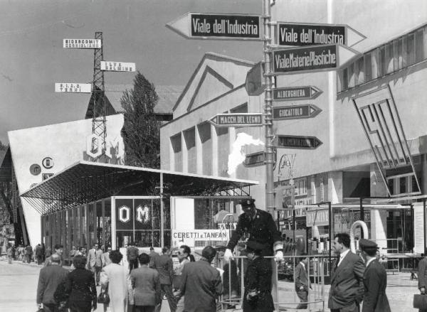 Fiera di Milano - Campionaria 1955 - Viale della siderurgia - Installazione segnaletica con vigile - Tettoia espositiva della Officine Meccaniche OM